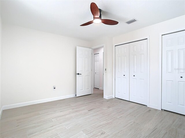 unfurnished bedroom featuring light wood-type flooring, multiple closets, baseboards, and ceiling fan