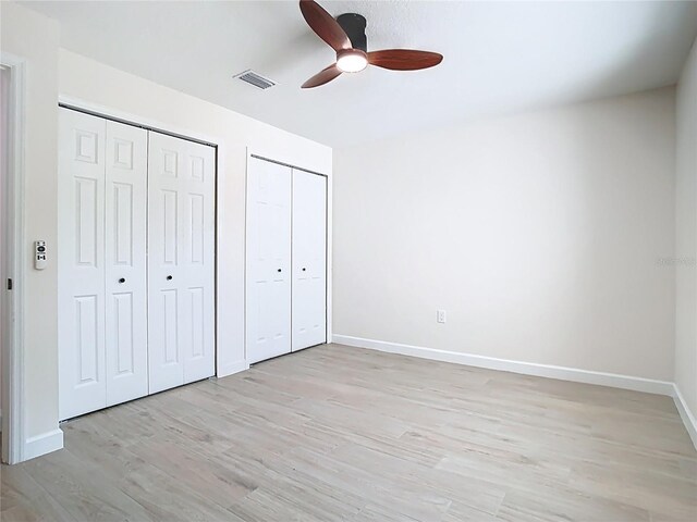 unfurnished bedroom with multiple closets, light wood finished floors, baseboards, and a ceiling fan
