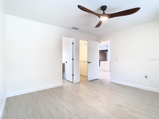 unfurnished bedroom featuring baseboards, a spacious closet, light wood-style flooring, a closet, and ceiling fan