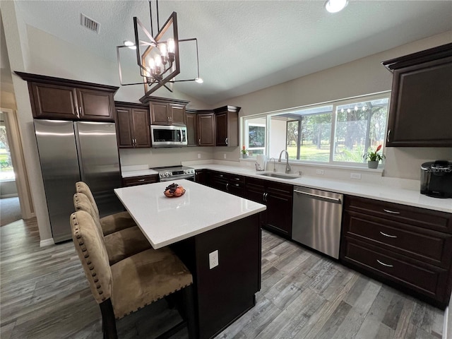 kitchen featuring appliances with stainless steel finishes, a sink, a textured ceiling, lofted ceiling, and visible vents