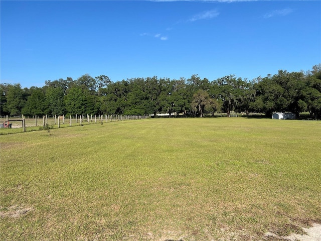 view of yard featuring a storage shed, fence, an outdoor structure, and a rural view