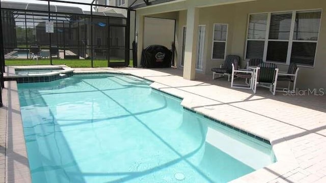 view of swimming pool with a patio, glass enclosure, and a pool with connected hot tub