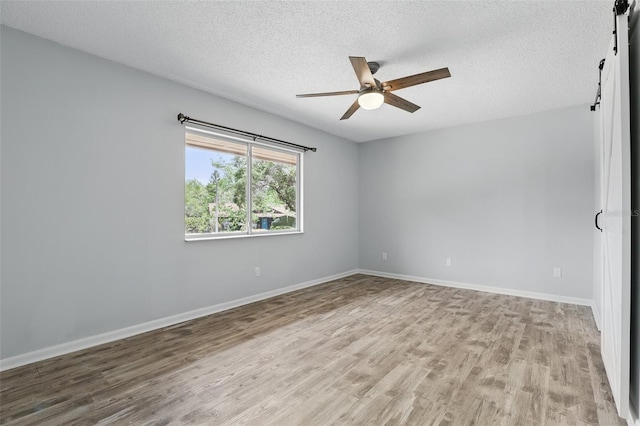 unfurnished room featuring wood finished floors, a ceiling fan, a textured ceiling, baseboards, and a barn door