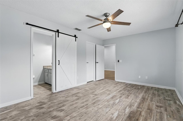 unfurnished bedroom featuring baseboards, visible vents, a barn door, and wood finished floors