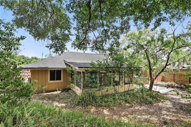 back of property with board and batten siding, roof with shingles, fence, and roof mounted solar panels