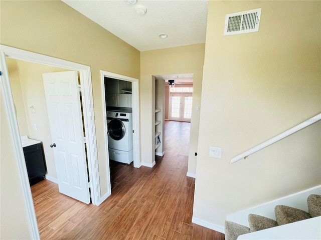 hallway featuring wood finished floors, visible vents, baseboards, washer / clothes dryer, and stairs