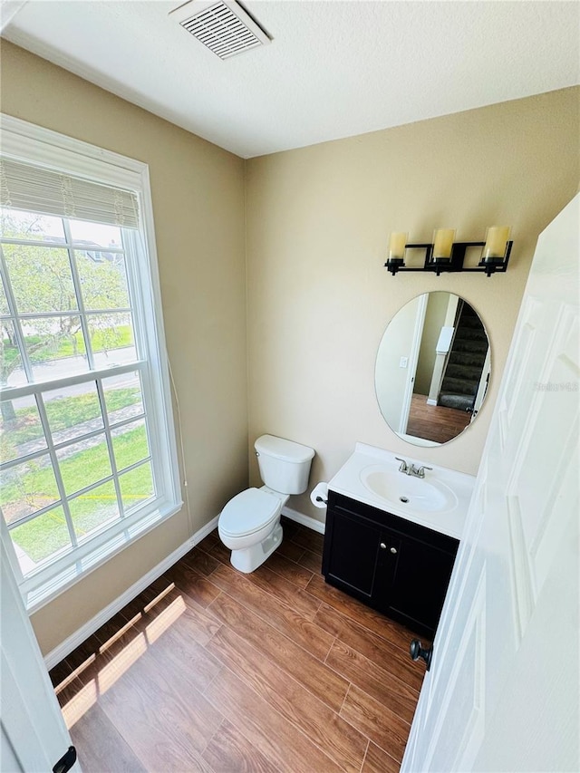 half bathroom featuring toilet, wood finished floors, a healthy amount of sunlight, visible vents, and baseboards