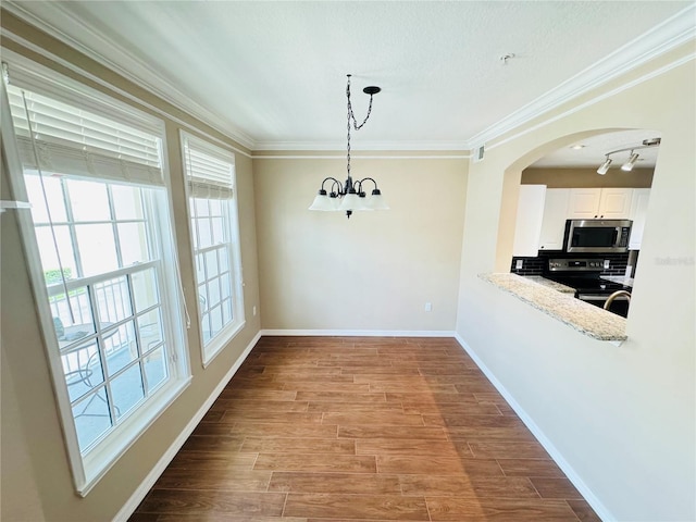 unfurnished dining area with a chandelier, baseboards, ornamental molding, wood finished floors, and arched walkways