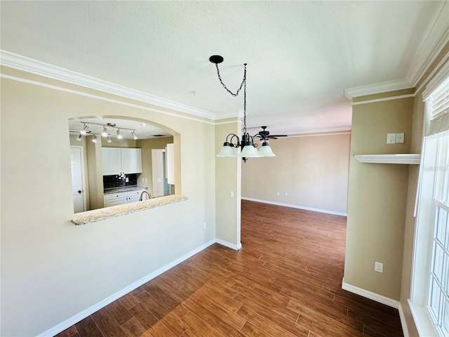 unfurnished dining area featuring an inviting chandelier, wood finished floors, crown molding, baseboards, and arched walkways