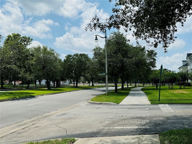 view of asphalt road featuring street lighting, curbs, and sidewalks