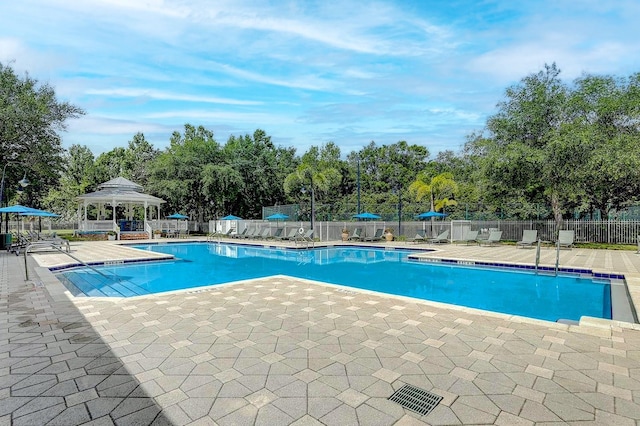 community pool with a gazebo, a patio, fence, and view of wooded area