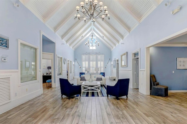 living area featuring a chandelier, high vaulted ceiling, light wood finished floors, beamed ceiling, and a wainscoted wall