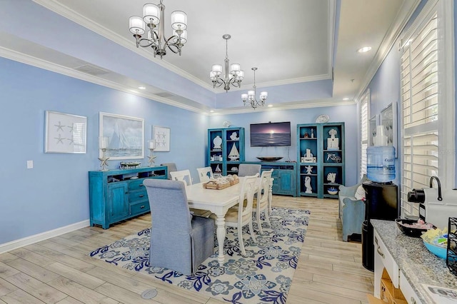 dining area with a chandelier, light wood-style flooring, crown molding, baseboards, and a tray ceiling