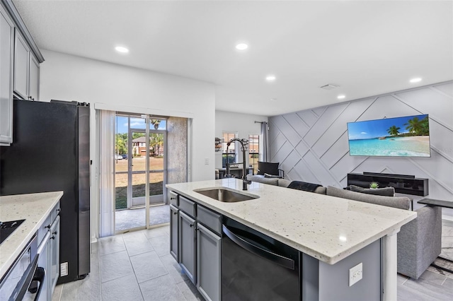 kitchen with light stone counters, a sink, dishwasher, freestanding refrigerator, and open floor plan