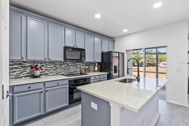 kitchen with light stone countertops, tasteful backsplash, a sink, black appliances, and gray cabinetry