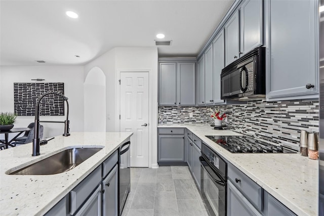 kitchen featuring visible vents, decorative backsplash, gray cabinets, a sink, and black appliances