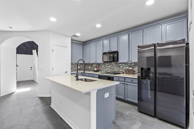 kitchen featuring decorative backsplash, arched walkways, light stone counters, a sink, and appliances with stainless steel finishes