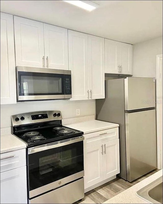 kitchen featuring light countertops, stainless steel appliances, light wood finished floors, and white cabinetry