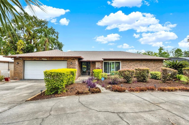 single story home with driveway, a shingled roof, brick siding, and an attached garage