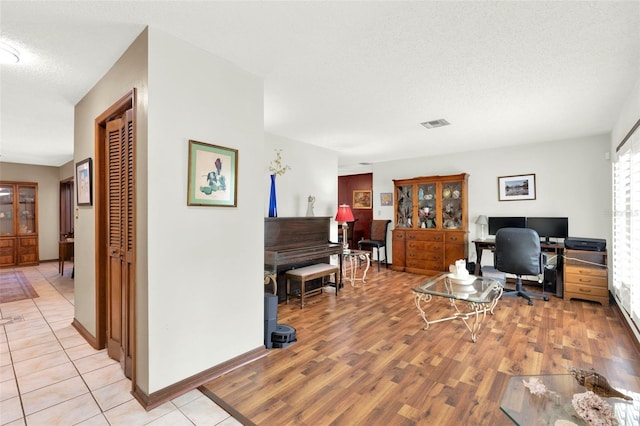 office area featuring light wood finished floors, a textured ceiling, baseboards, and visible vents