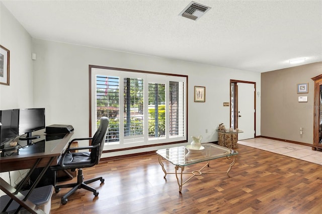 home office with a textured ceiling, baseboards, visible vents, and wood finished floors