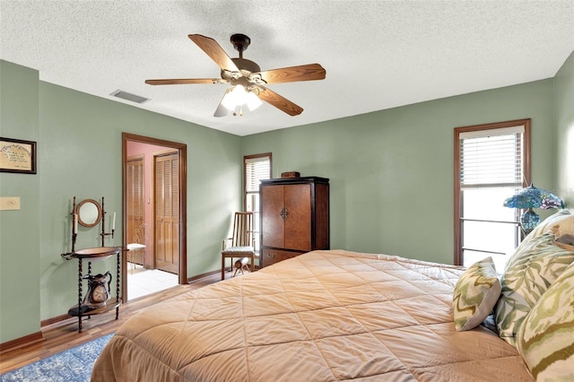 bedroom with wood finished floors, a textured ceiling, visible vents, ceiling fan, and baseboards