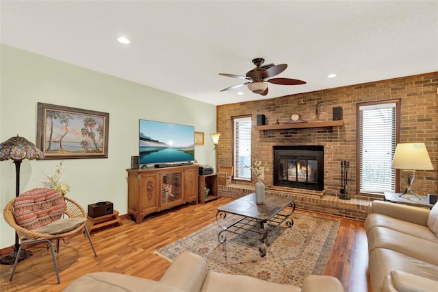living area with brick wall, ceiling fan, light wood-style flooring, and a fireplace