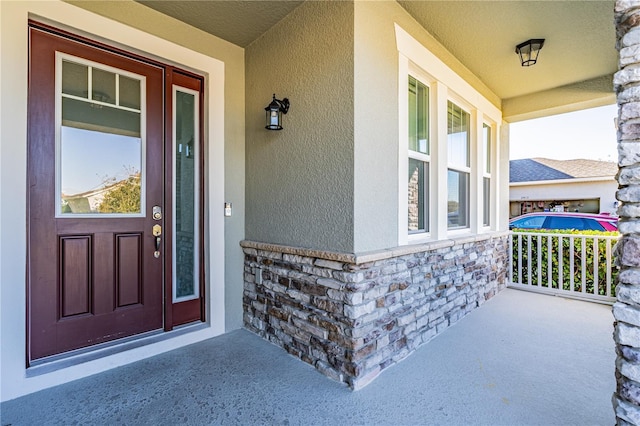 property entrance with stone siding, a porch, and stucco siding