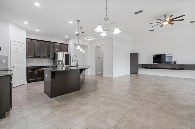 kitchen with dark brown cabinets, visible vents, open floor plan, dark stone countertops, and stainless steel refrigerator with ice dispenser