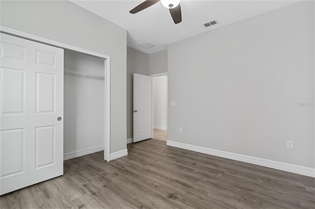 unfurnished bedroom featuring a ceiling fan, a closet, baseboards, visible vents, and wood finished floors