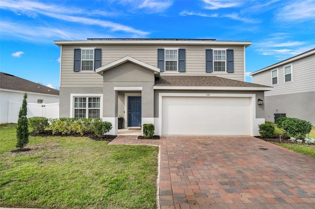 traditional-style home featuring a front lawn, fence, stucco siding, roof mounted solar panels, and an attached garage