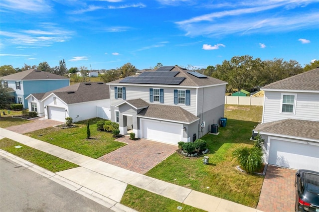 traditional-style house featuring a front lawn, fence, decorative driveway, a shingled roof, and roof mounted solar panels