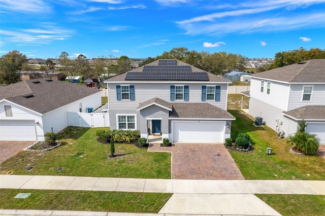 traditional home with a gate, central air condition unit, decorative driveway, fence, and roof mounted solar panels