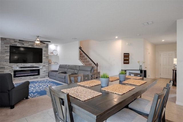 dining room with ceiling fan, a large fireplace, stairs, light tile patterned floors, and visible vents