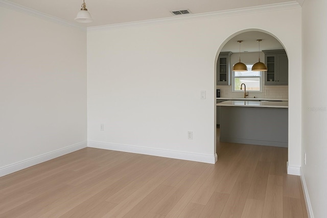 empty room featuring a sink, ornamental molding, light wood-type flooring, arched walkways, and baseboards
