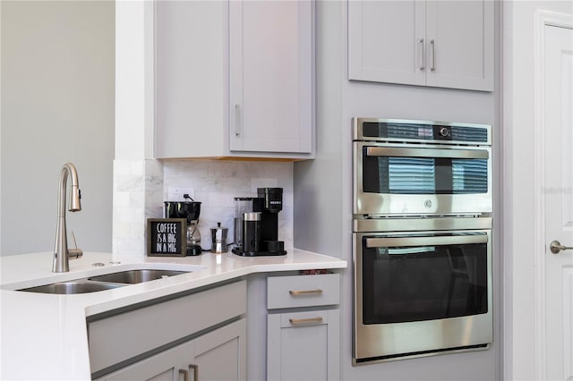 kitchen featuring double oven, a sink, light countertops, and tasteful backsplash