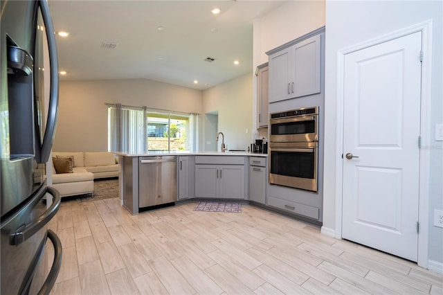 kitchen with gray cabinets, vaulted ceiling, a peninsula, open floor plan, and stainless steel appliances