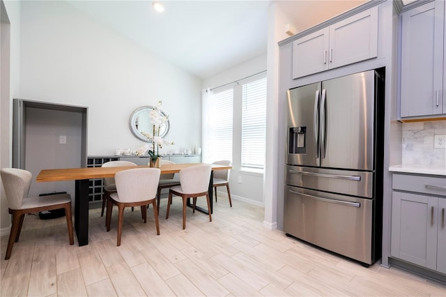 dining room featuring baseboards, light wood-style floors, and vaulted ceiling