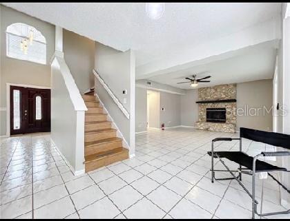 foyer entrance with a stone fireplace, stairs, a ceiling fan, baseboards, and light tile patterned floors