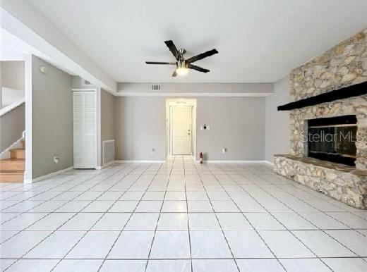 unfurnished living room with ceiling fan, tile patterned flooring, a stone fireplace, visible vents, and stairway