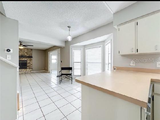 kitchen featuring a fireplace, light countertops, white cabinetry, a ceiling fan, and light tile patterned floors