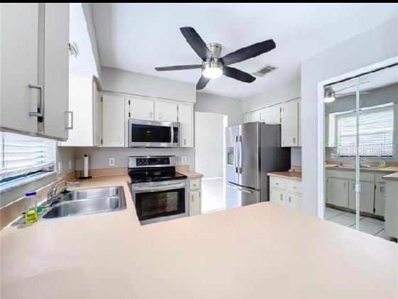 kitchen with a ceiling fan, light countertops, white cabinetry, a sink, and stainless steel appliances