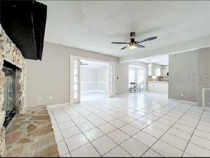 unfurnished living room with baseboards, ceiling fan, a stone fireplace, and light tile patterned floors