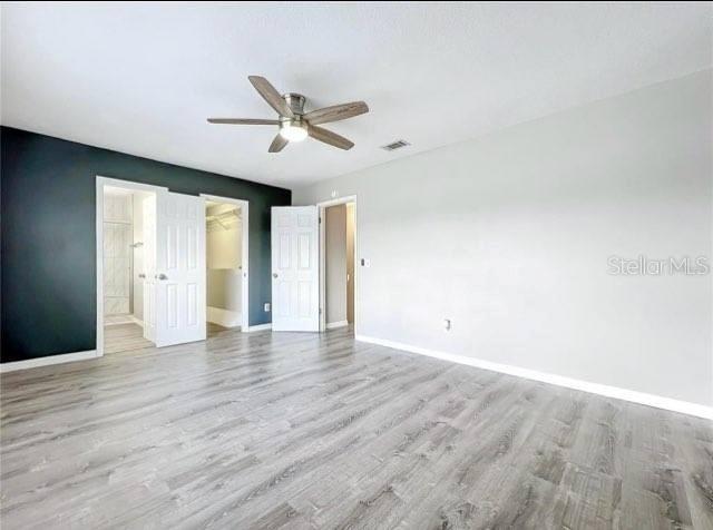 unfurnished bedroom with a walk in closet, baseboards, visible vents, and wood finished floors