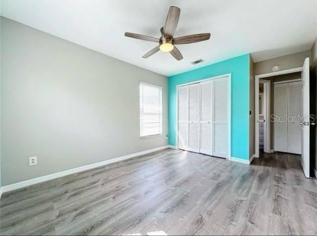 unfurnished bedroom featuring a closet, visible vents, wood finished floors, baseboards, and ceiling fan