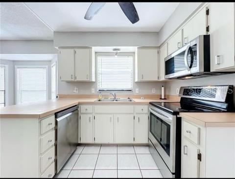 kitchen with appliances with stainless steel finishes, a sink, light countertops, a peninsula, and light tile patterned flooring