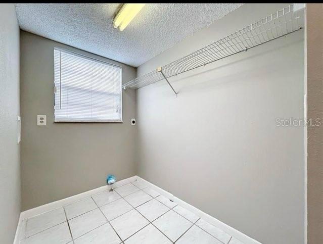 clothes washing area featuring laundry area, baseboards, a textured ceiling, tile patterned floors, and electric dryer hookup