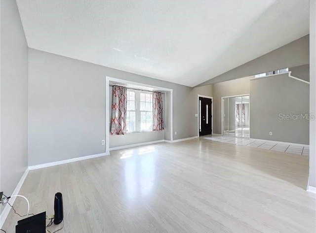 unfurnished living room with baseboards, lofted ceiling, and wood finished floors