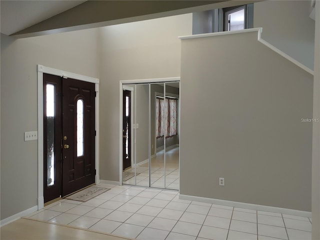 entryway featuring light tile patterned flooring, baseboards, a healthy amount of sunlight, and lofted ceiling