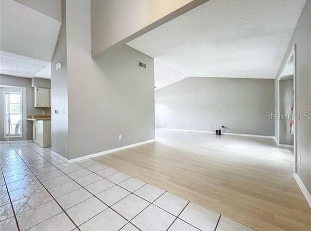 spare room with visible vents, baseboards, light tile patterned floors, and lofted ceiling